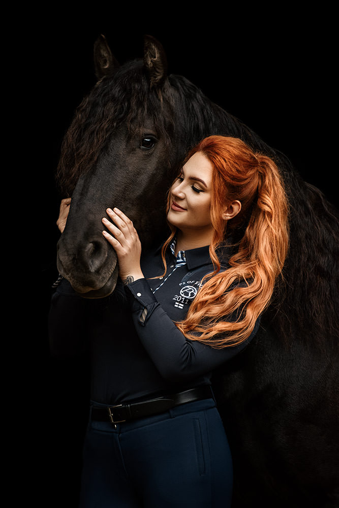 Eine Frau mit roten Haaren kuschelt liebevoll mit einem schwarzen Pferd
