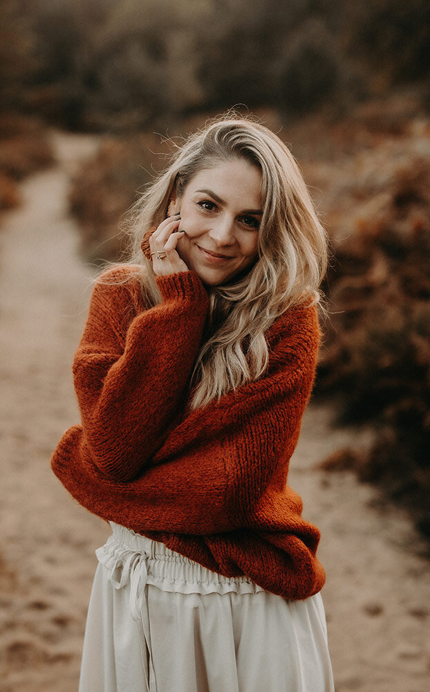 Stephanie Hafner, Pferdefotografin aus der Schweiz, im rostroten Strickpulli auf einem herbstlichen Sandweg